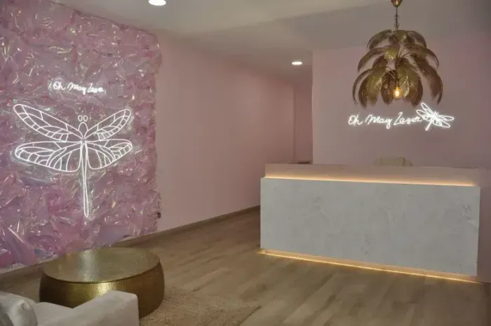 Zona de recepción rosa con un mostrador blanco, un letrero de neón con una mariposa y detalles dorados