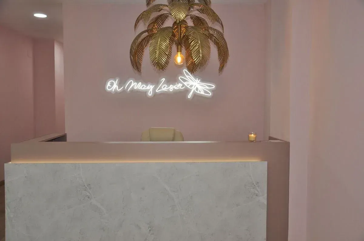 Elegante mostrador de recepción con paredes rosas, decoración de palmeras doradas y un letrero luminoso