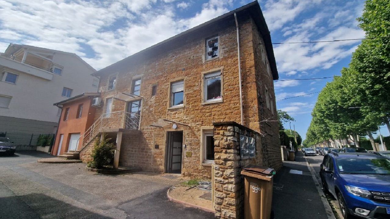 Bâtiment en pierre avec rue sur la droite et véhicules garés