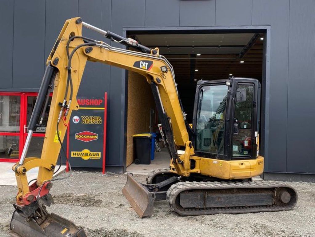 Vor einem Gebäude steht ein kleiner Bagger.