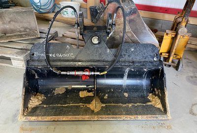 Auf dem Boden steht ein Eimer mit einem daran befestigten Hydrauliksystem.