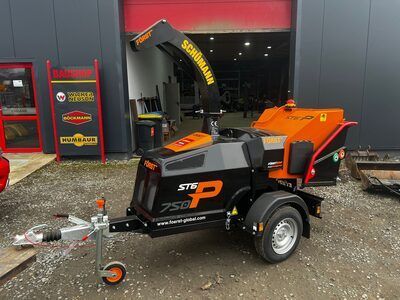 Eine schwarz-orangefarbene Maschine auf einem Anhänger steht vor einem Gebäude.