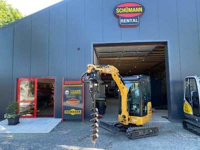 Vor einem Gebäude parkt ein kleiner gelber Bagger.