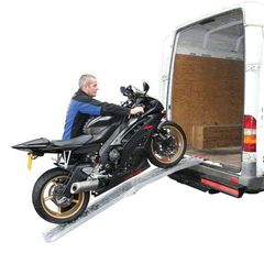 Un hombre está cargando una motocicleta en una rampa hacia una camioneta.