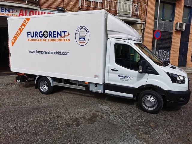 Una furgoneta blanca está estacionada al costado de la carretera frente a un edificio.
