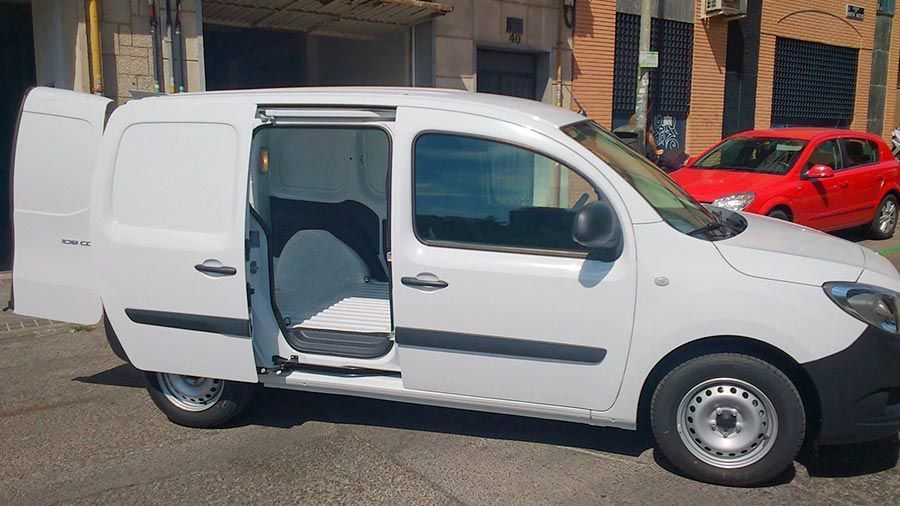 Una furgoneta blanca con las puertas abiertas está estacionada frente a un edificio.