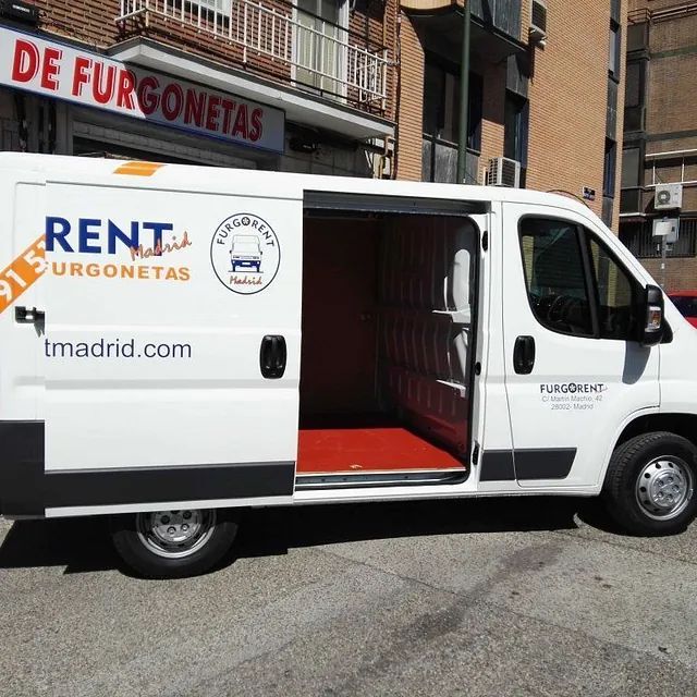 Una furgoneta de alquiler blanca está estacionada frente a un edificio.