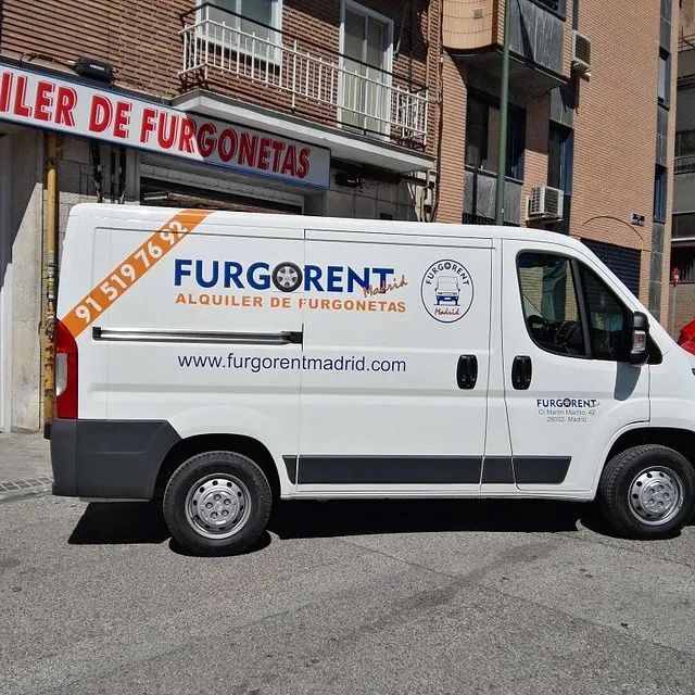Una furgoneta blanca de Furgorent está estacionada frente a un edificio.