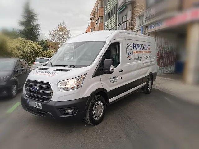 Una camioneta blanca está estacionada al costado de la carretera frente a un edificio.