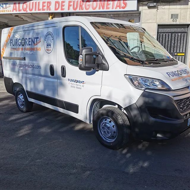Una furgoneta blanca está estacionada frente a un cartel que dice alquiler de furgonetas