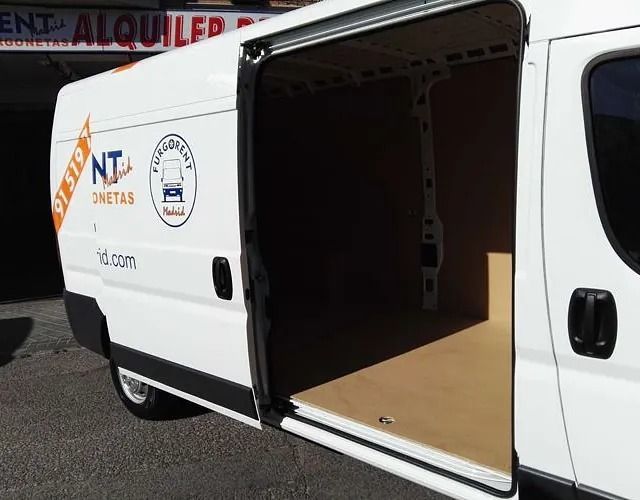 Una furgoneta blanca con la puerta abierta está estacionada frente a un edificio.