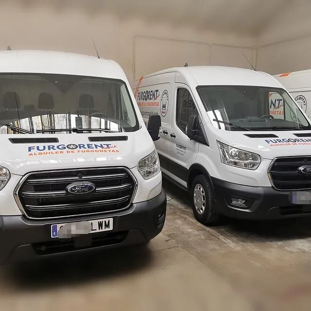 Dos furgonetas blancas están aparcadas una al lado de la otra en un garaje.