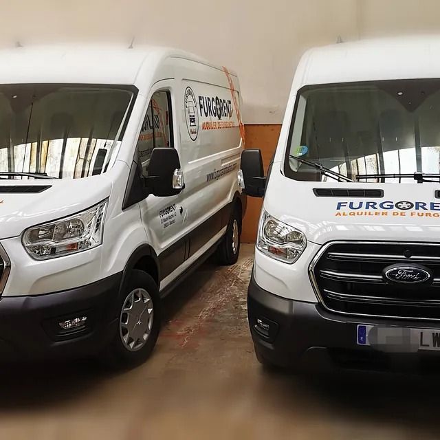 Dos furgonetas blancas están aparcadas una al lado de la otra en un garaje.