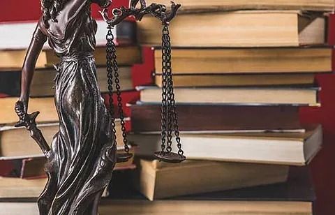 Estatua de la Dama de la Justicia con balanza y espada, frente a una pila de libros de leyes.