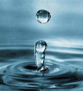 Gota de agua cayendo, creando una salpicadura en forma de corona en el agua, fondo azul.