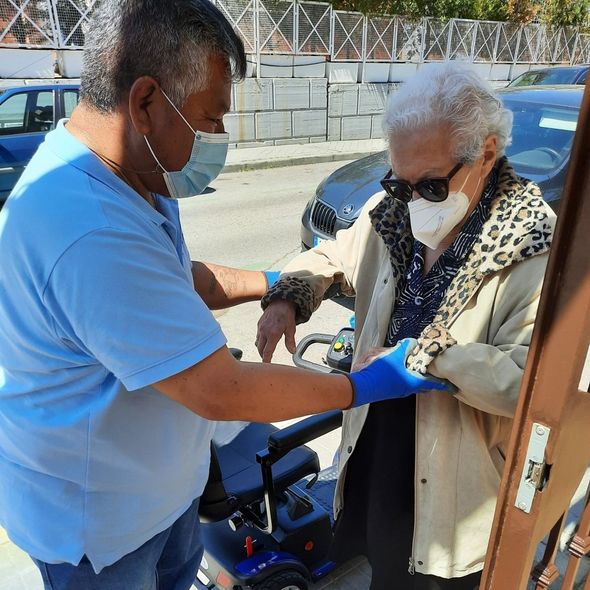 Un hombre con una máscara está ayudando a una anciana en silla de ruedas.