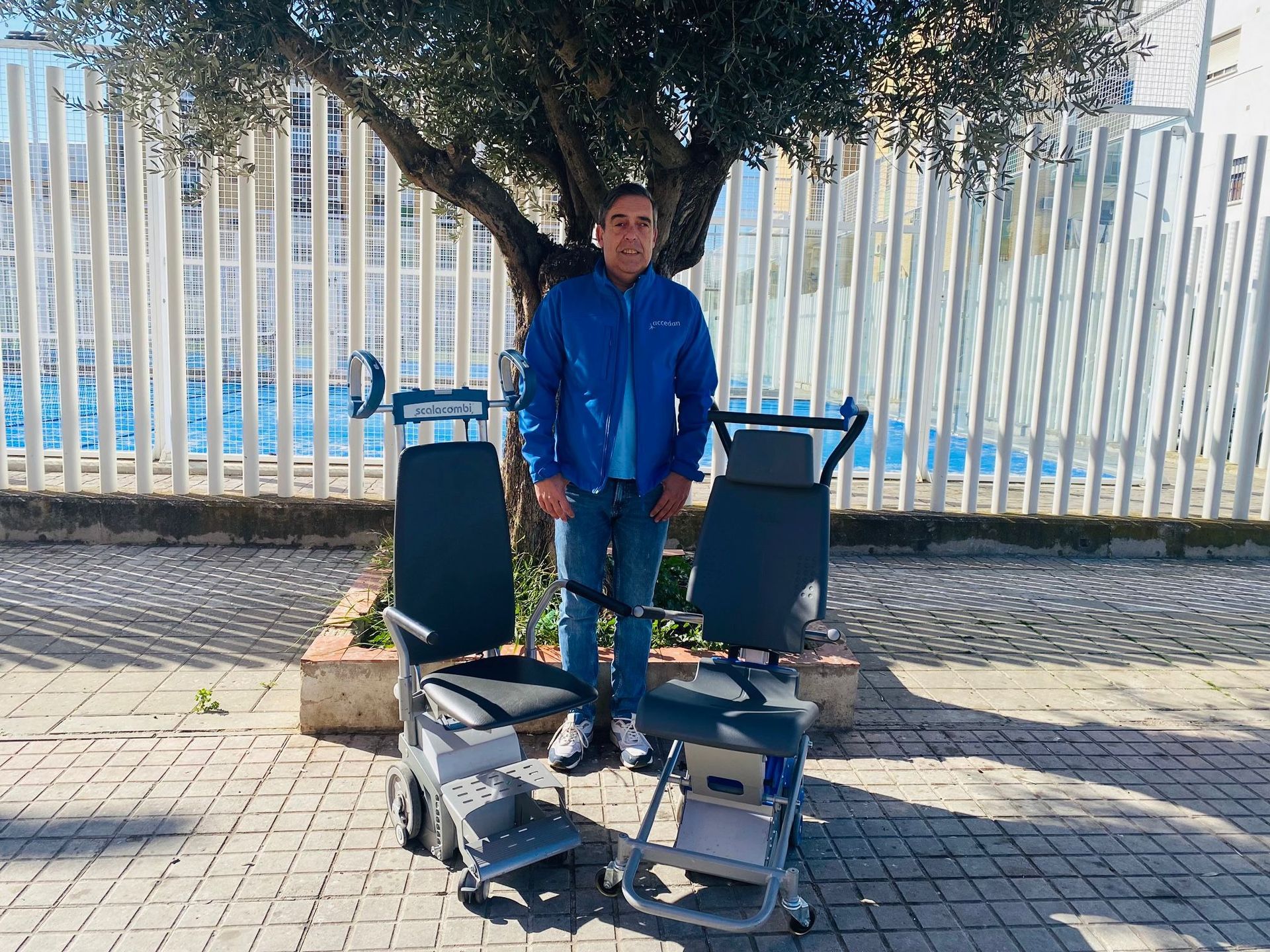 Un hombre con una chaqueta azul está de pie junto a dos sillas.