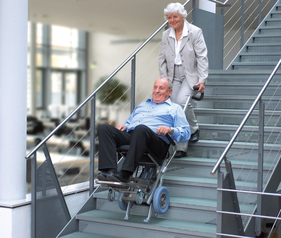Un hombre en silla de ruedas es empujado por una mujer por las escaleras.