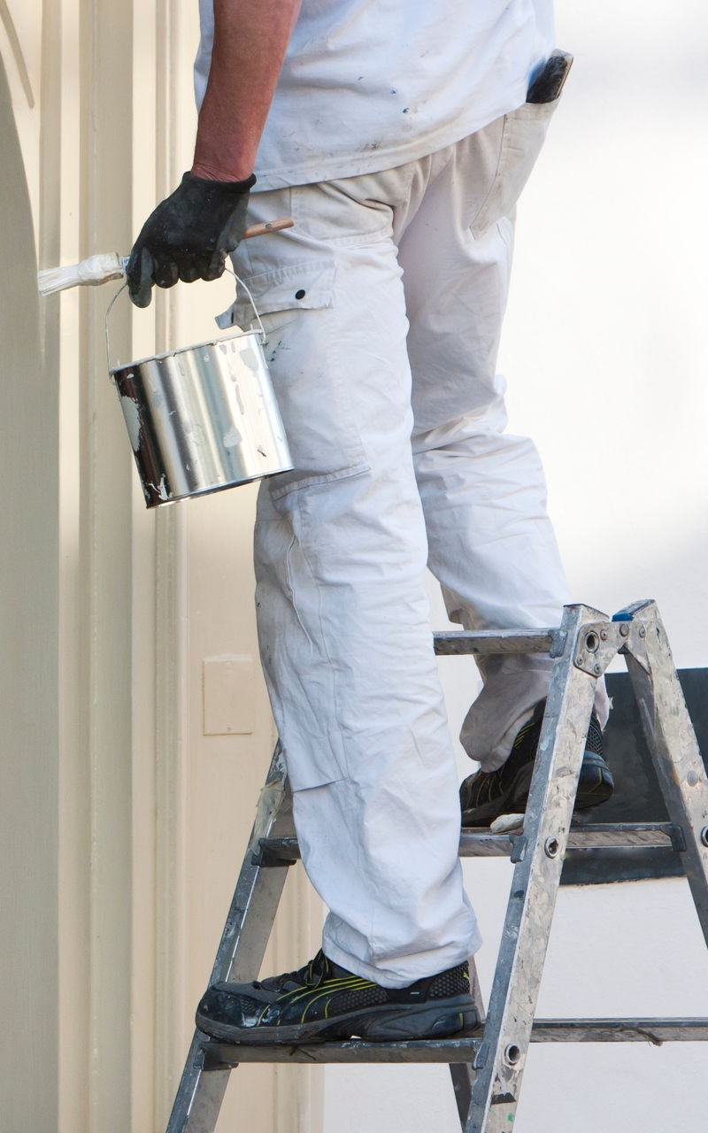 Un peintre en tenue de travail tenant un pot de peinture et un pinceau.