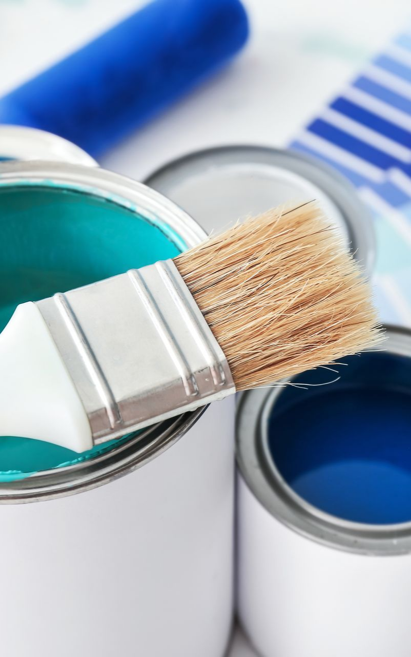 Des pots de peinture ouverts avec des rouleaux et des pinceaux à proximité.