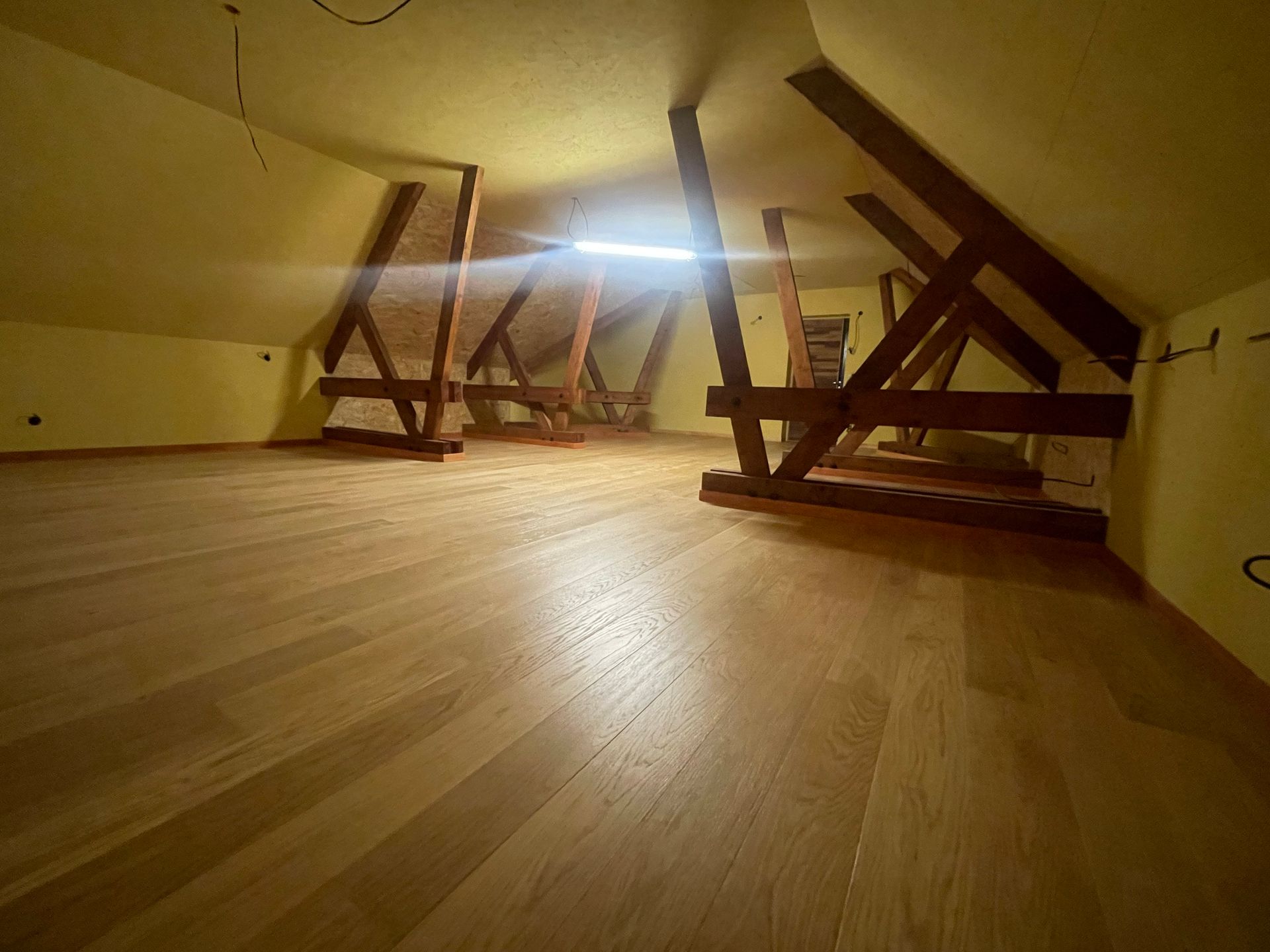 Un grenier aménagé avec un sol en bois clair et des poutres apparentes.