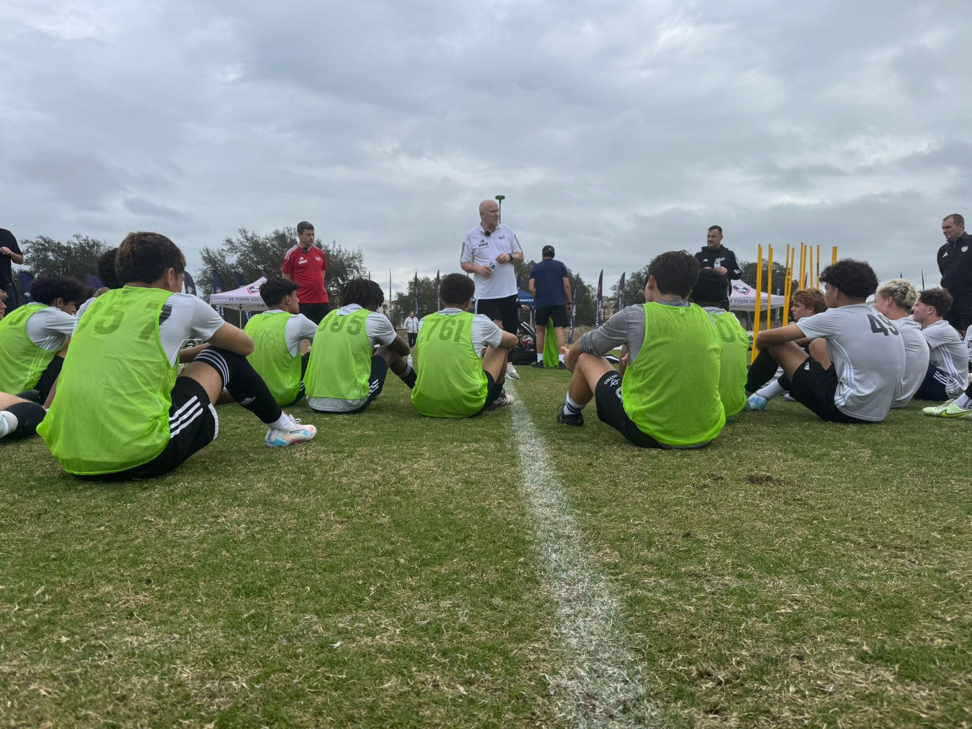 A group of soccer players are sitting on the grass listening to a coach