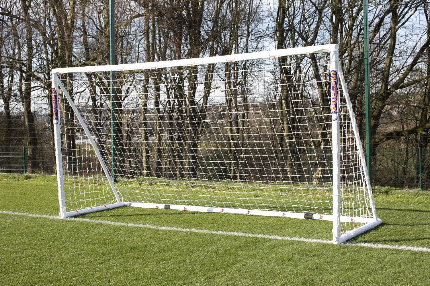 A soccer goal on a field with trees in the background