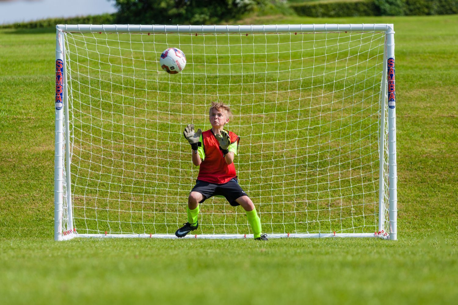 A young boy in a red shirt and green socks is playing soccer