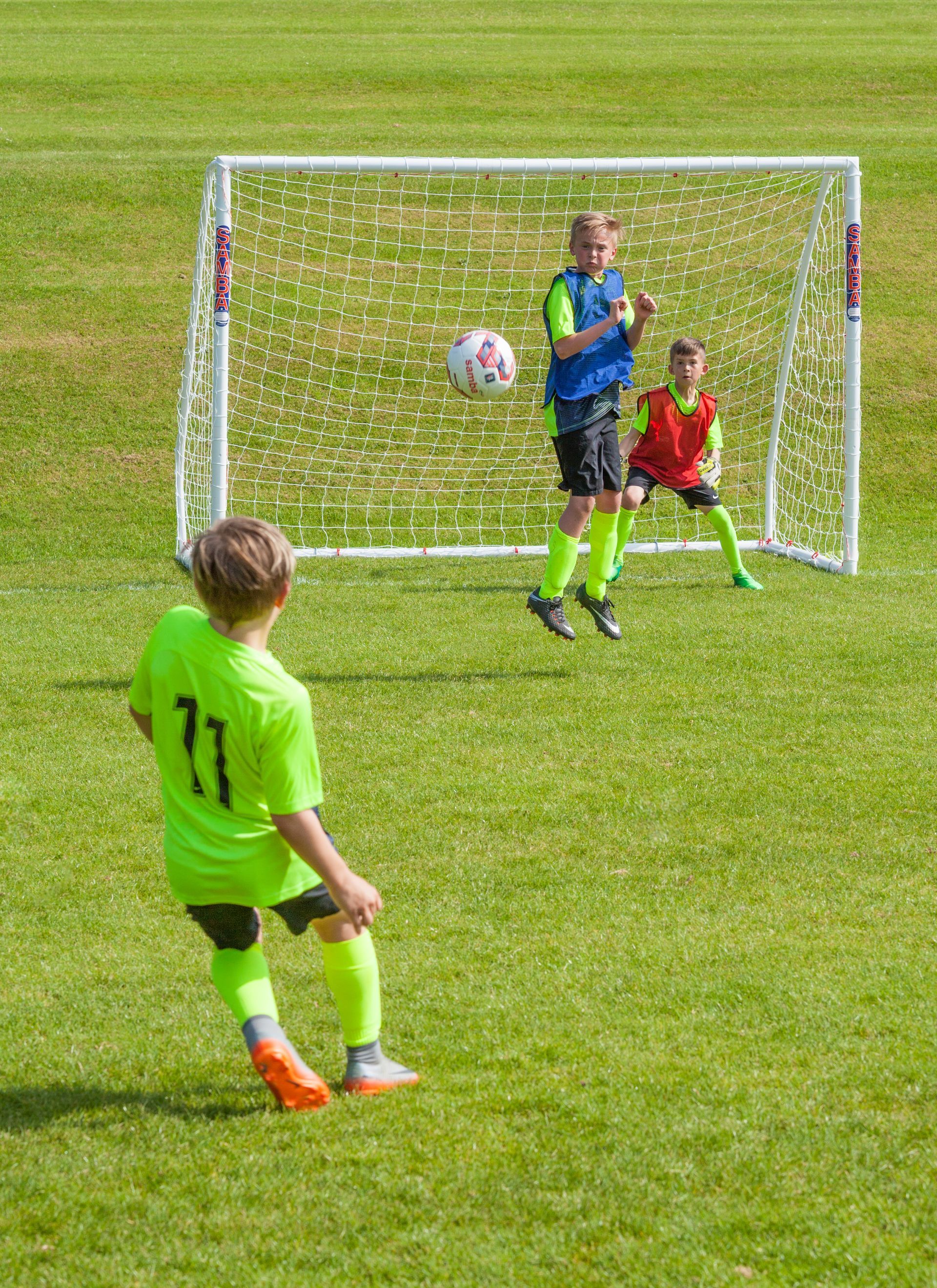 A boy in a green shirt with the number 77 on it kicks a soccer ball
