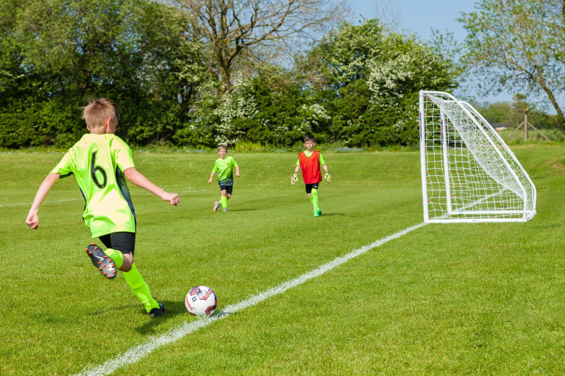A boy in a green shirt with the number 77 on it kicks a soccer ball