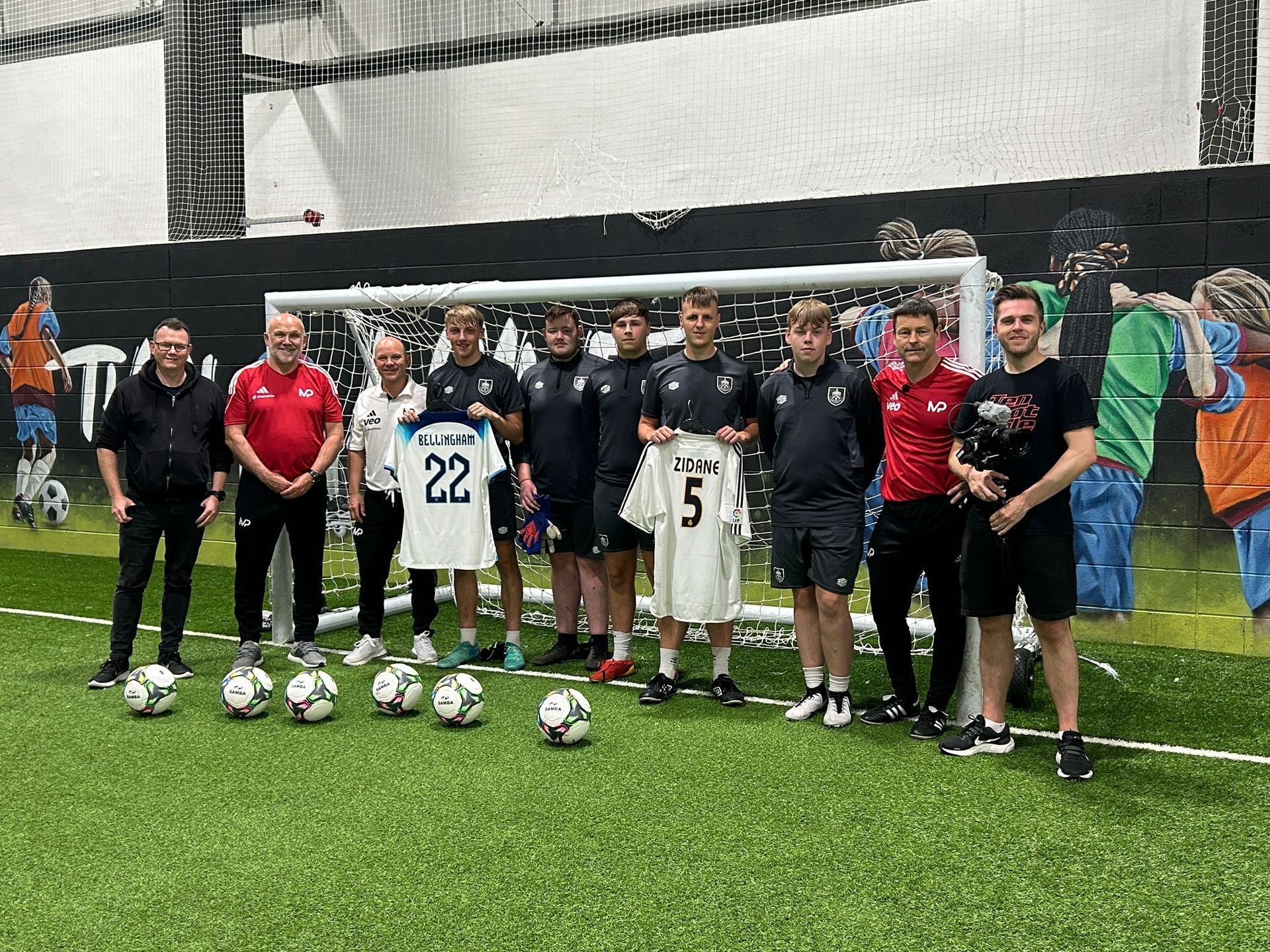A group of men are standing on a soccer field holding soccer balls and jerseys.