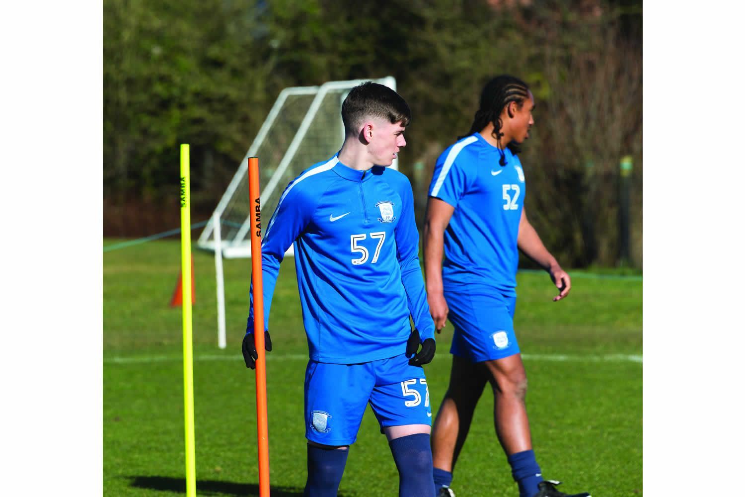 Two soccer players are walking on a field and one has the number 57 on his shirt