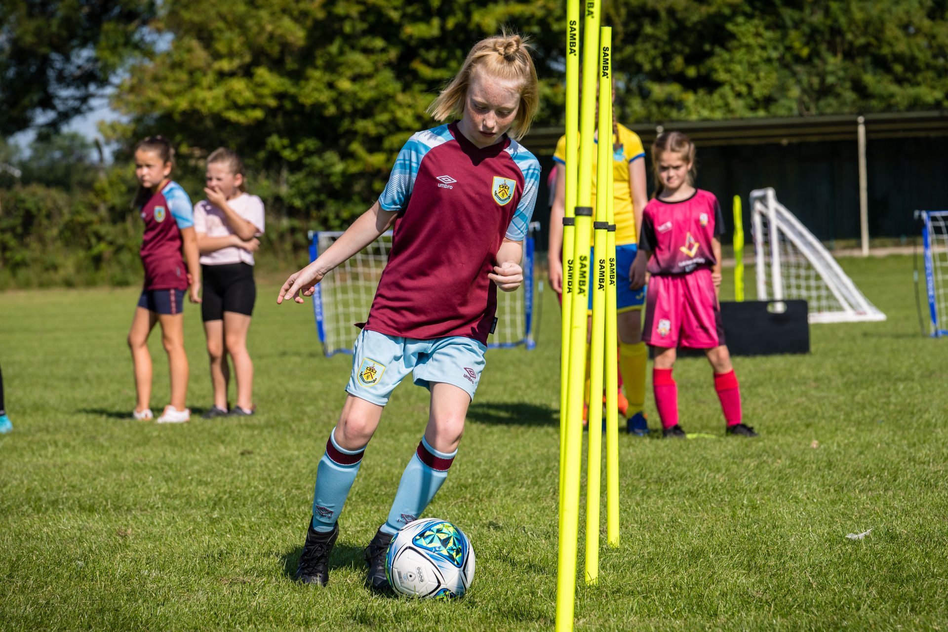A young girl in a maroon shirt is kicking a soccer ball