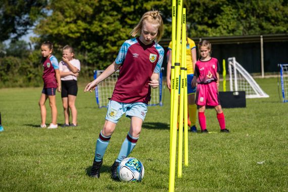 A young girl in a maroon shirt is kicking a soccer ball