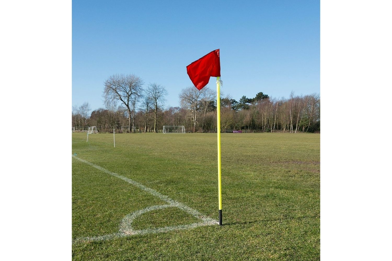 A red flag on a yellow pole on a soccer field