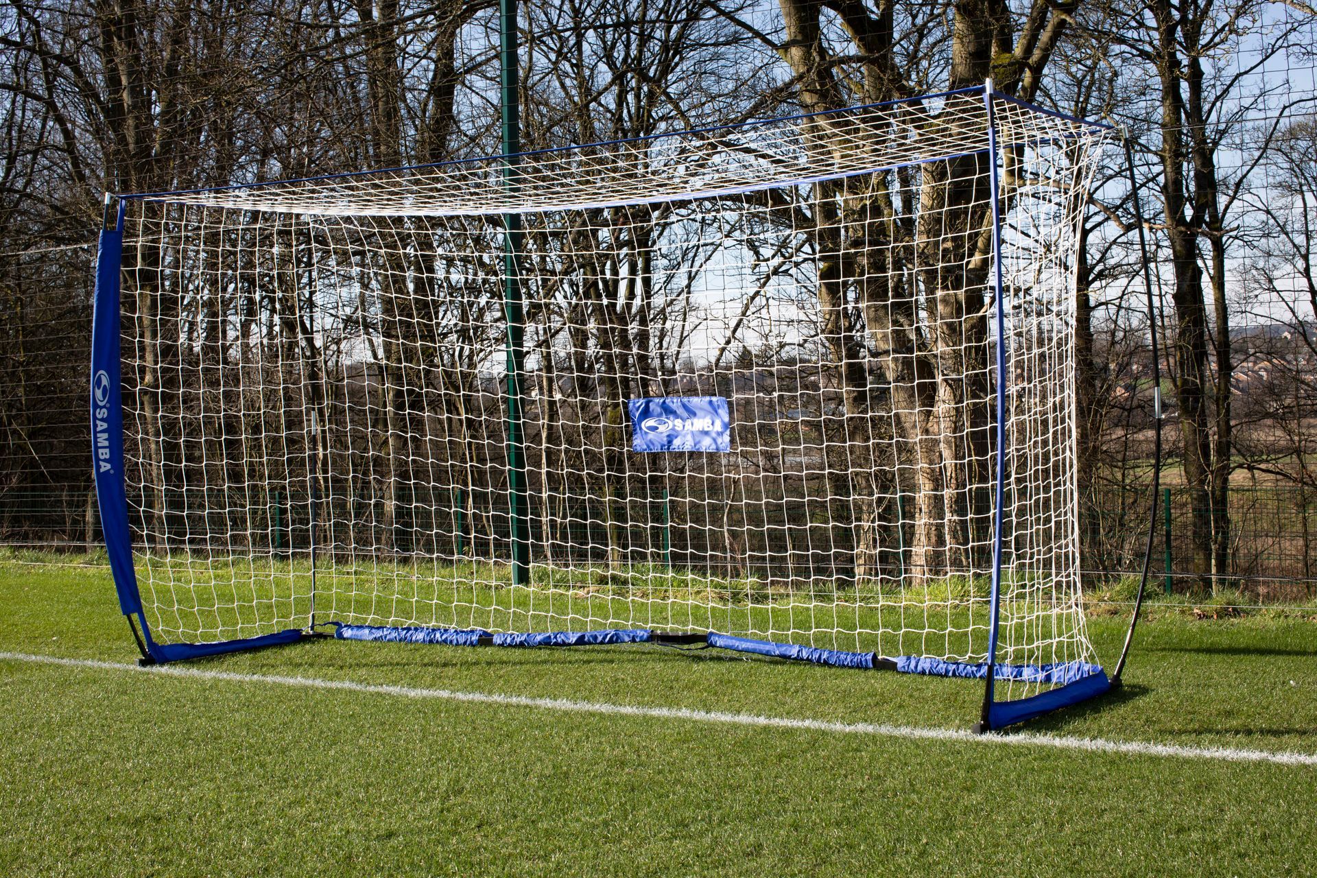 A soccer goal on a field with trees in the background