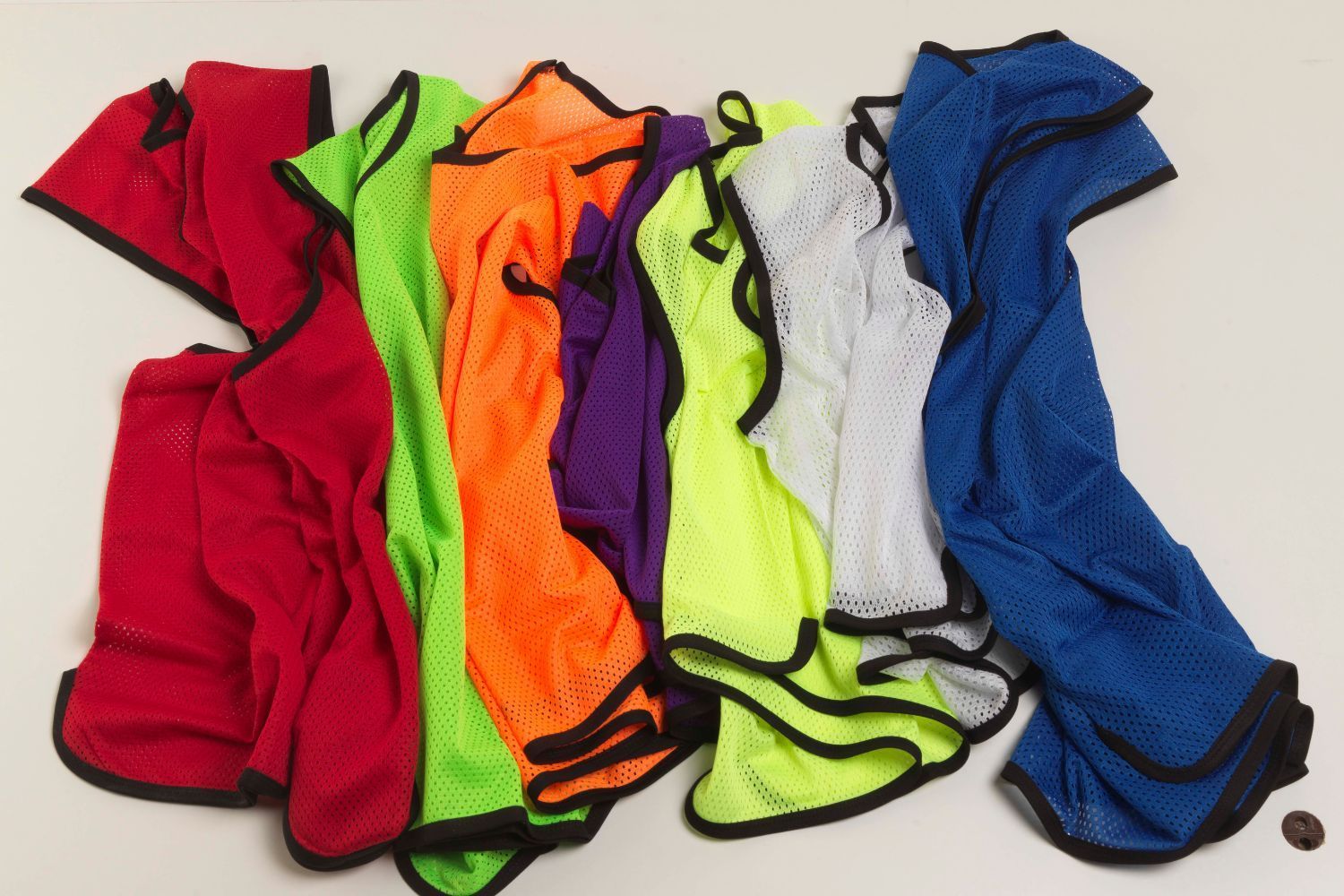 A bunch of different colored mesh vests are stacked on top of each other