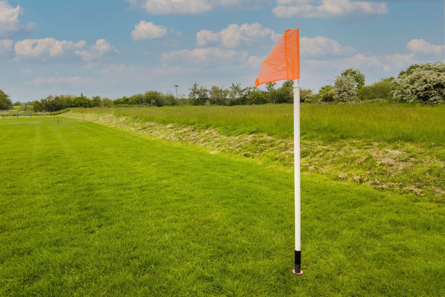 An orange flag on a white pole in a grassy field