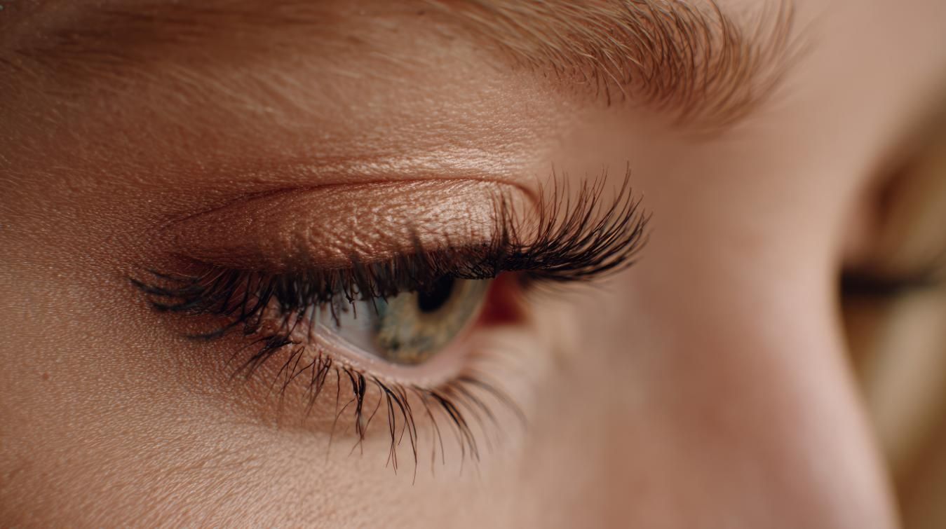 Primer plano de un ojo con pestañas largas y sombra de ojos; el ojo es verde con piel marrón claro.