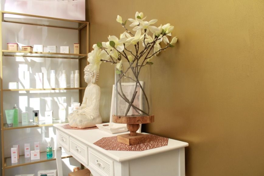 Consola blanca con jarrón de flores blancas, estatua de Buda y estantería. Pared dorada.