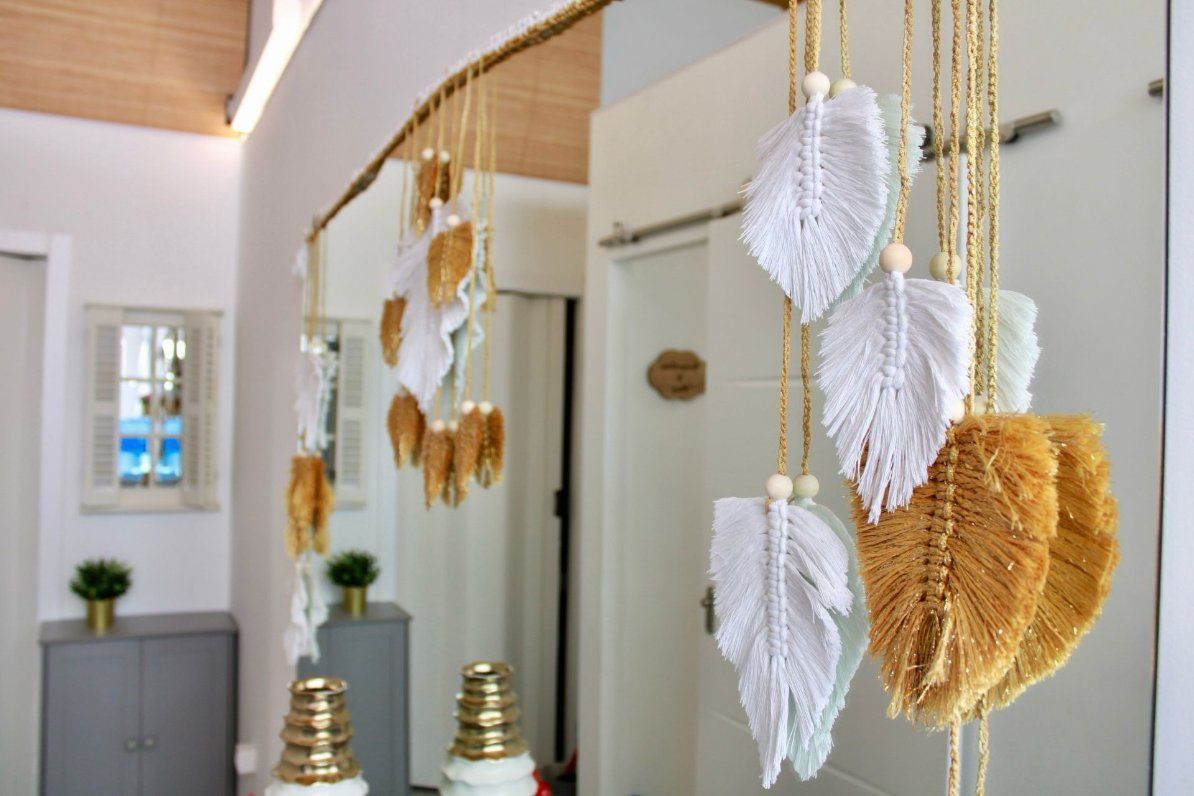 Adornos de plumas de macramé colgando de una rama de madera, exhibidos en una habitación bien iluminada.