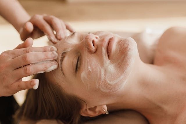 Persona que recibe un tratamiento facial con las manos aplicando espuma en la cara; ojos cerrados.