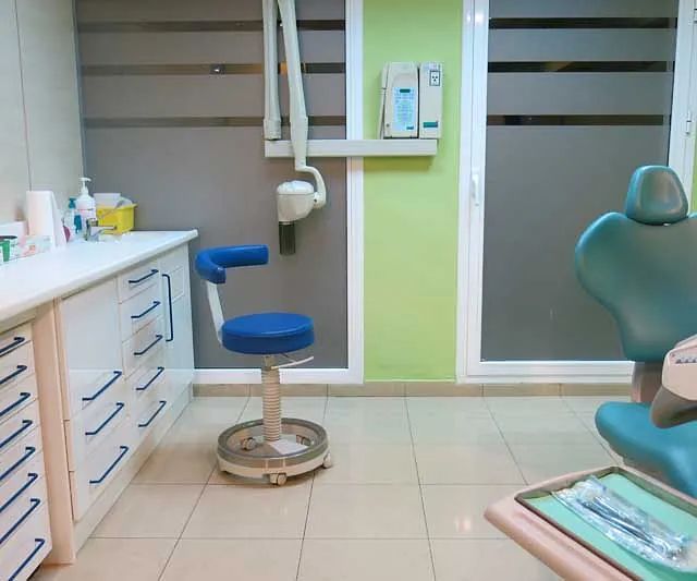 Un consultorio dental con una silla azul y una pared verde.