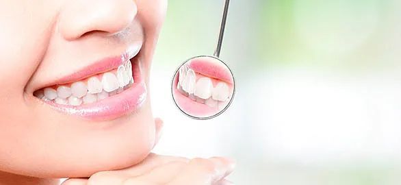 Una mujer sonríe mientras se mira los dientes en un espejo.