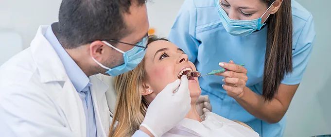 Un dentista y una enfermera están examinando los dientes de una mujer en un consultorio dental.