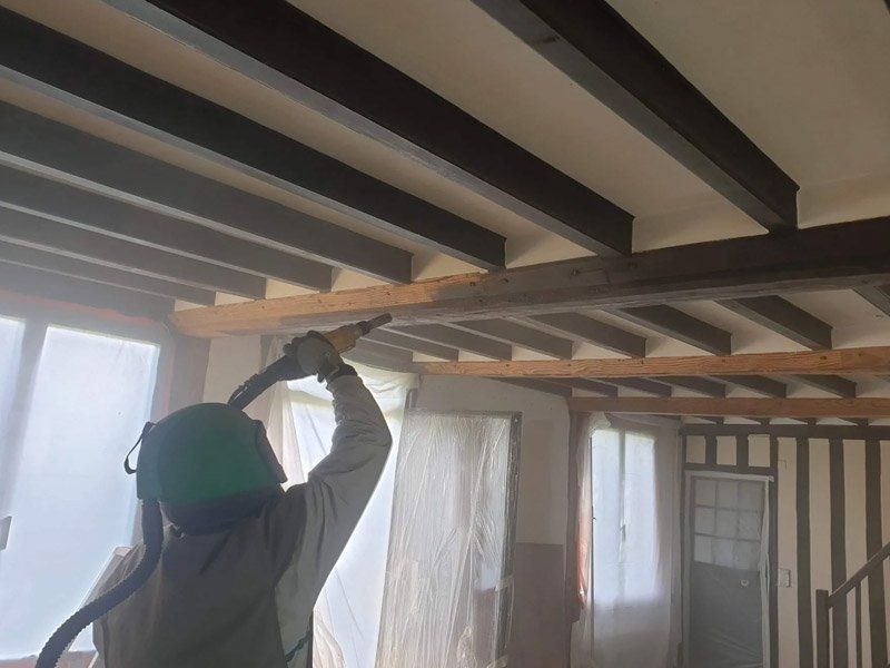 Une personne aérogommant des poutres