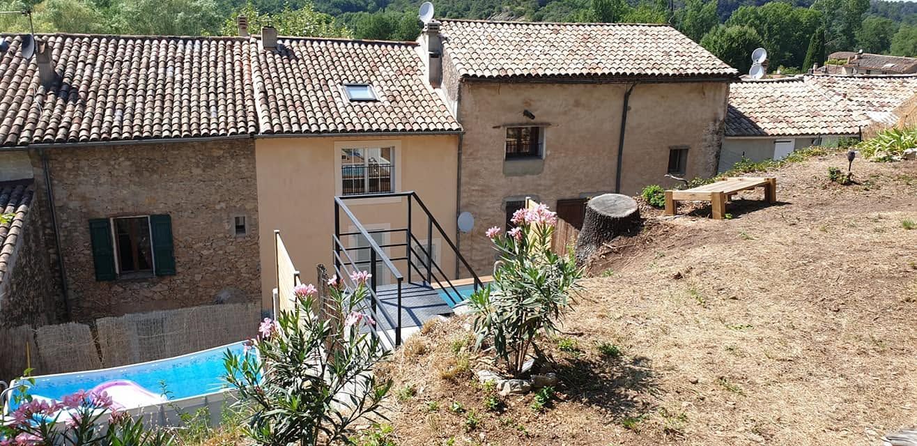 Maisons en pierre aux toits de tuiles, sur un coteau, avec un petit patio, une piscine et de la verdure devant.