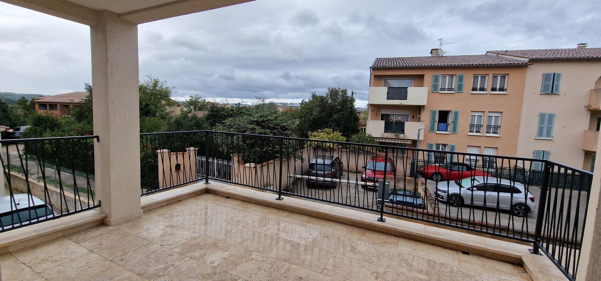 Vue depuis un balcon donnant sur une rue et des immeubles d'habitation par temps couvert.