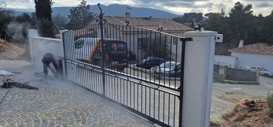 Portail en métal noir avec à l'extérieur, une personne en combinaison de protection.