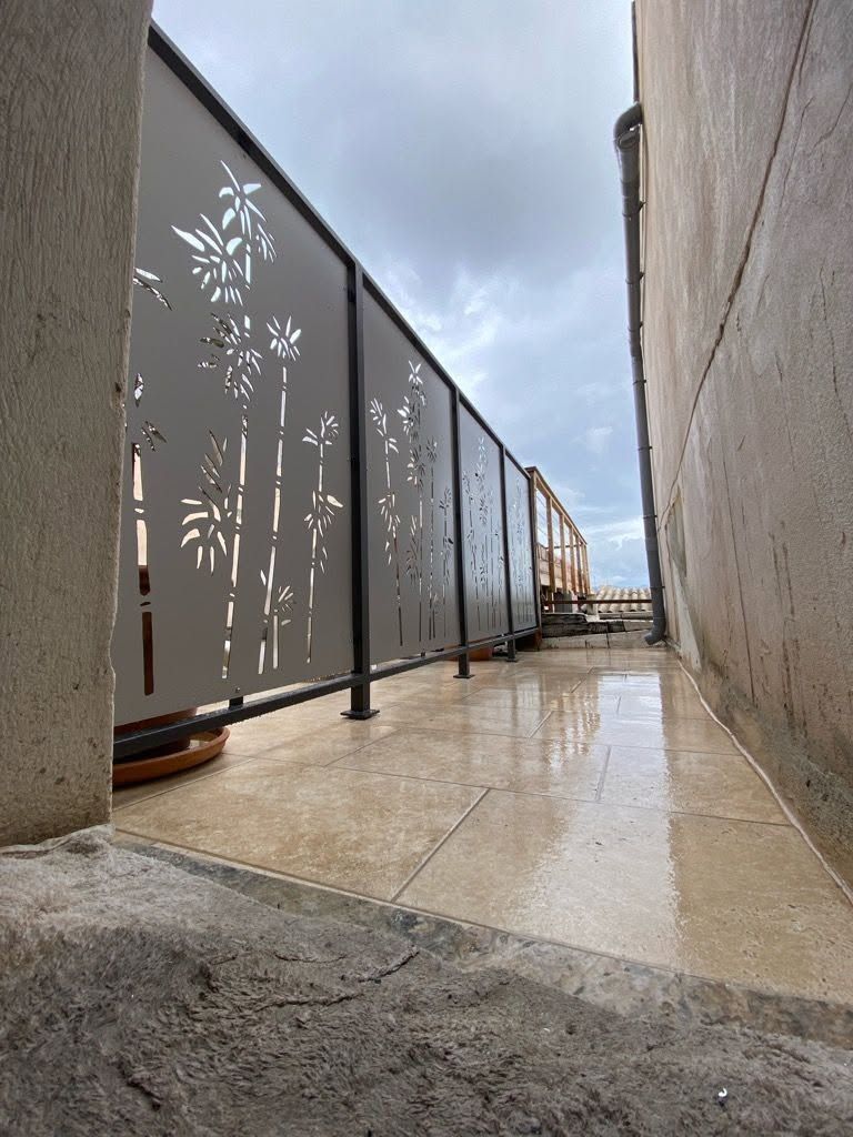 Passerelle étroite sur le toit avec une rambarde métallique décorative, des murs en béton sur un sol mouillé.